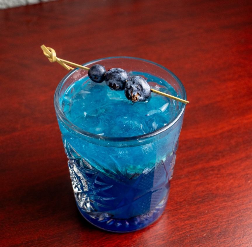 Coctel azul con moras sobre mesa de laca roja